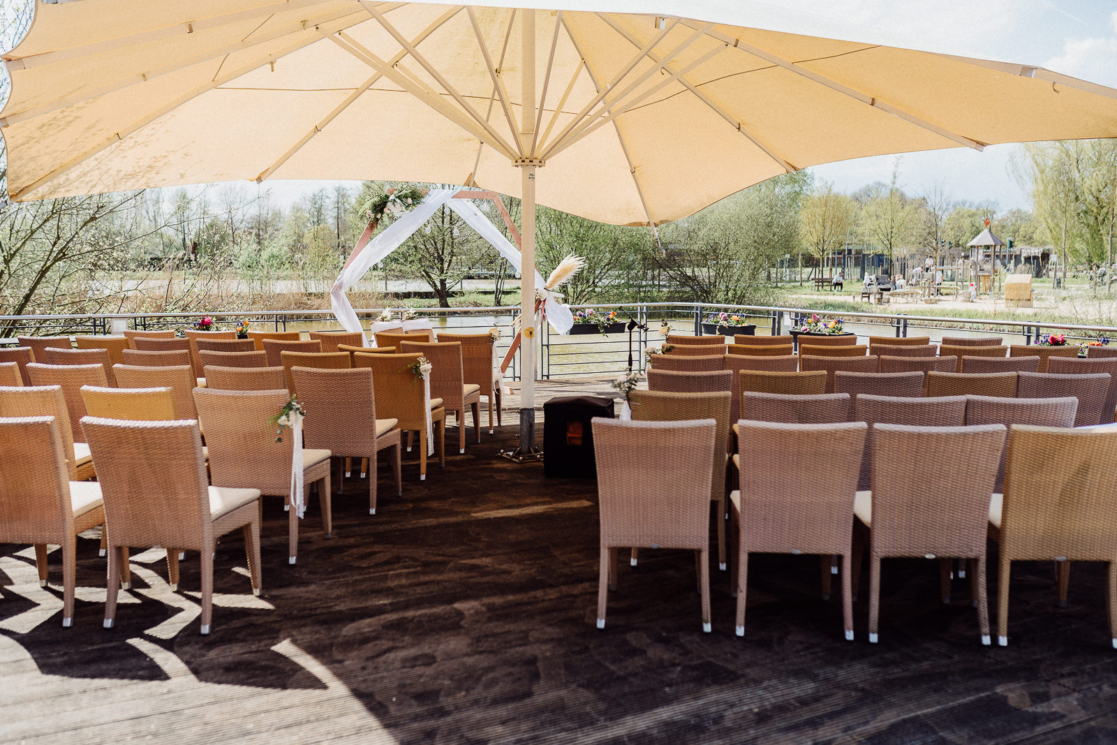 Stuhlreihen und ein Schirm auf einem Holzsteg über einem See für eine freie Trauung in Rietberg.