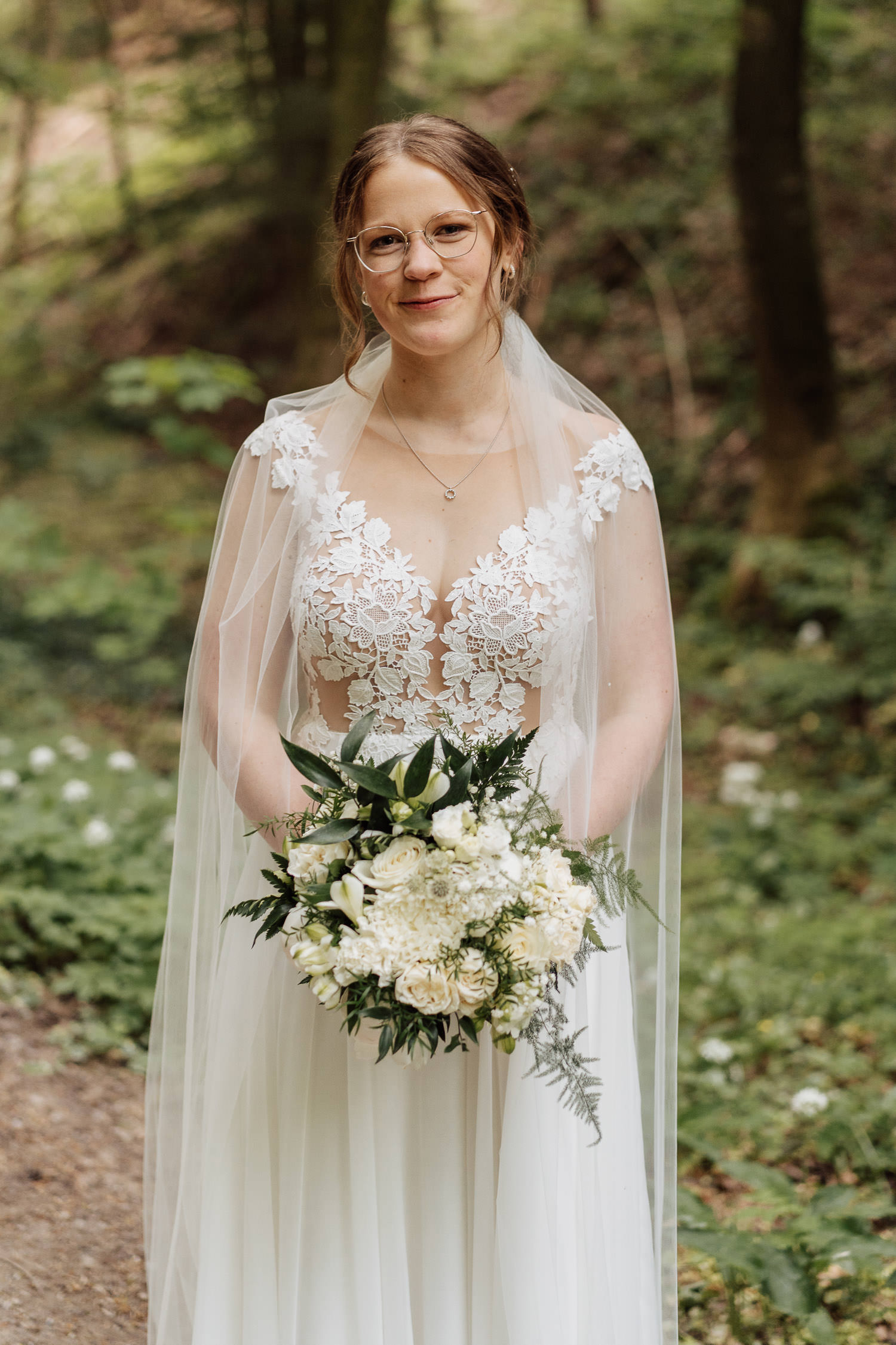 Eine Braut mit Schleier steht im Teutoburger Wald und schaut in die Kamera. Sie hält ihren Brautstrauß.