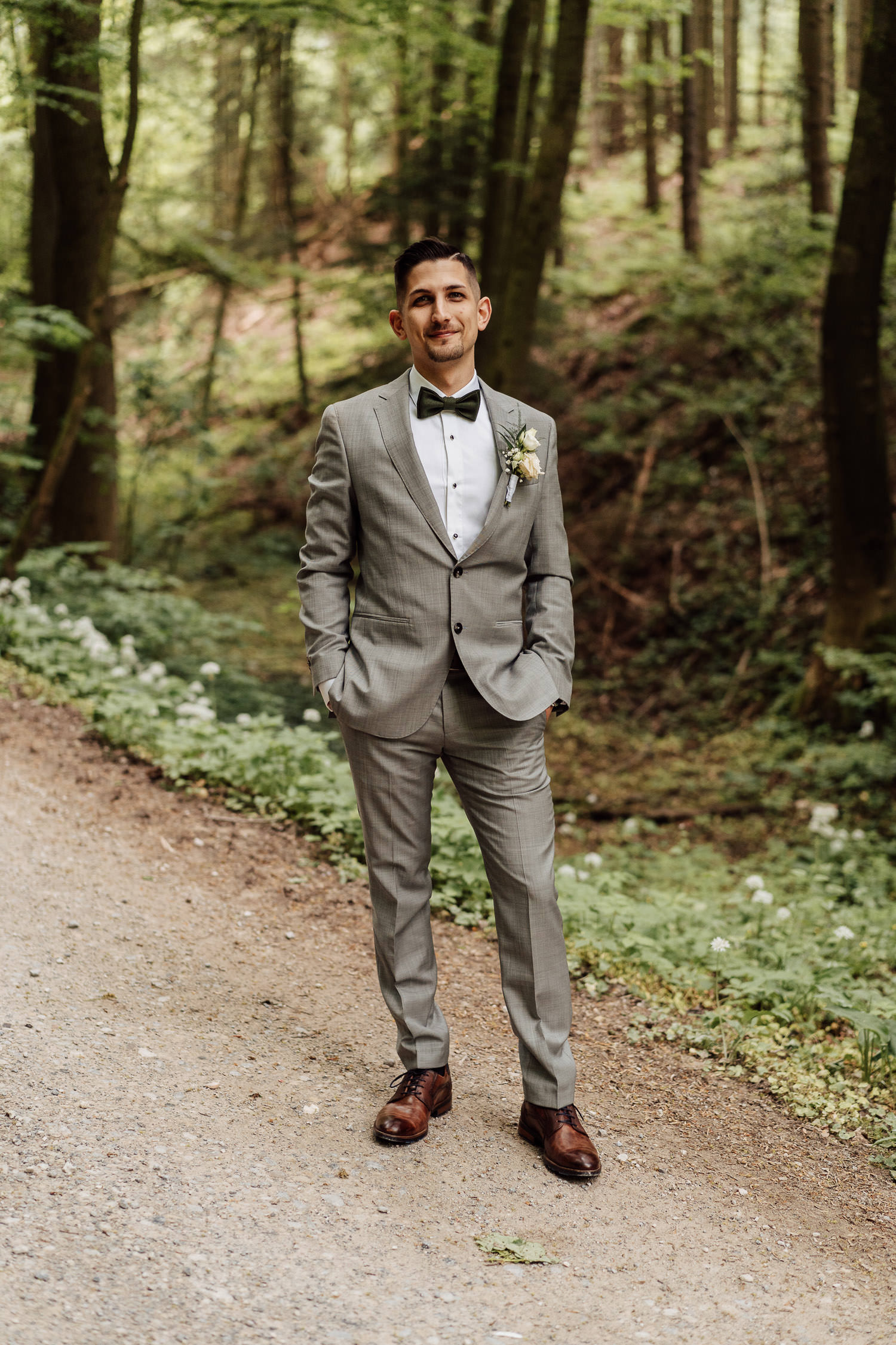 Bräutigam in grauem Anzug mit Fliege und braunen Lederschuhe im Wald bei Outdoor Hochzeit an der Waterboer Bielefeld. 