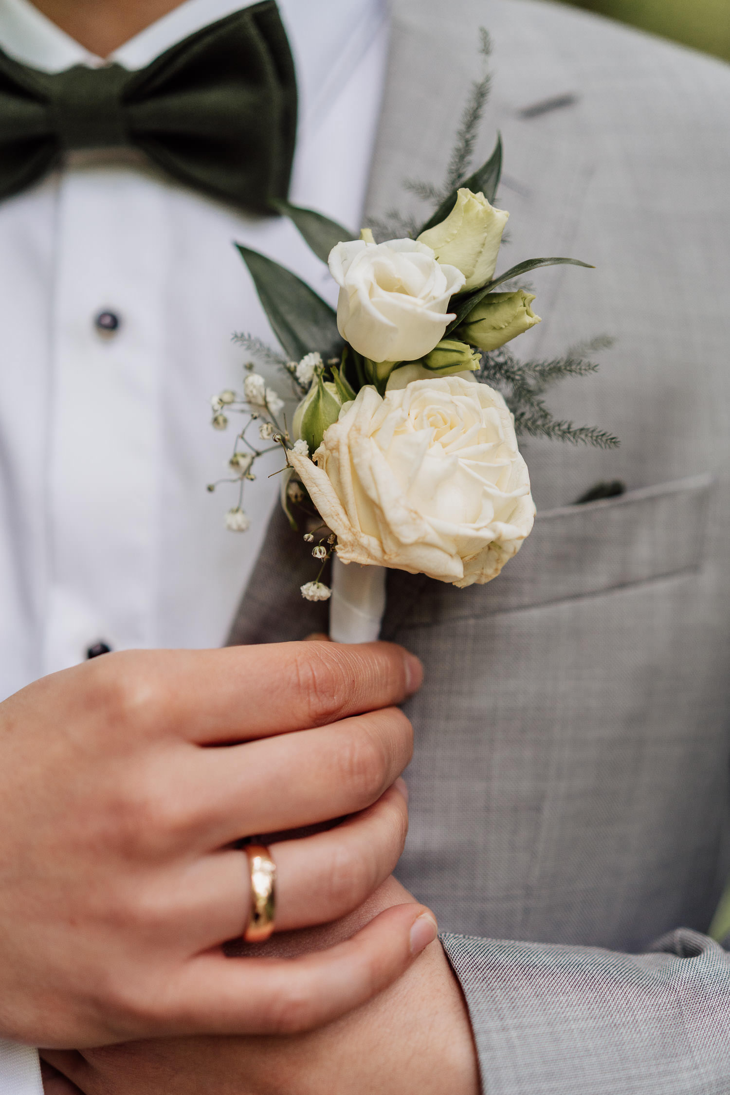 Weiße Rose als Anstecksträußchen beim Bräutigam mit grauem Anzug.